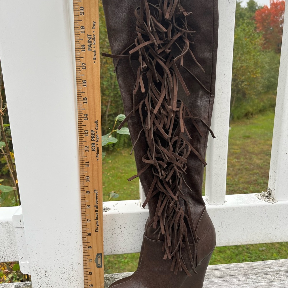 Knee high brown leather wedge boot with fringe detail.
